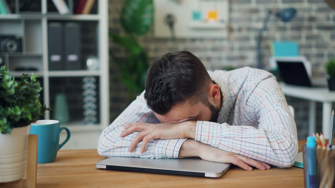 Ein Mann ist am Schreibtisch vor dem Laptop eingeschlafen